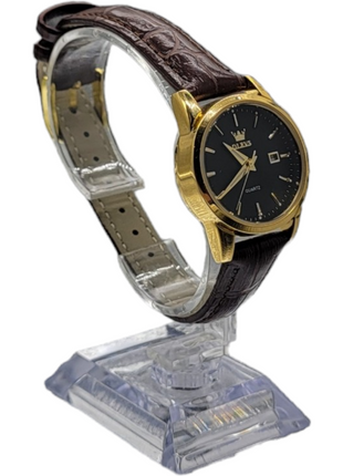 A gold and black wristwatch with a brown leather strap on a display stand.