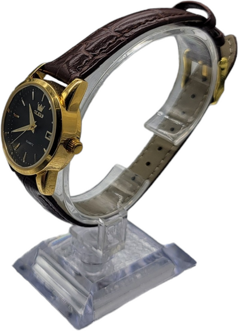 Gold-tone wristwatch with a black dial and brown leather strap on a clear display stand